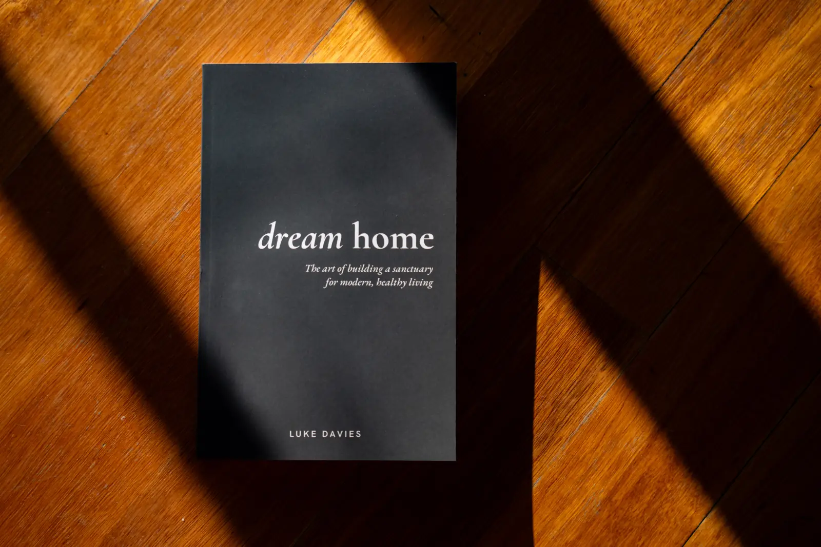 The Dream Home paperback on a timber floor, cut across by shafts of afternoon light