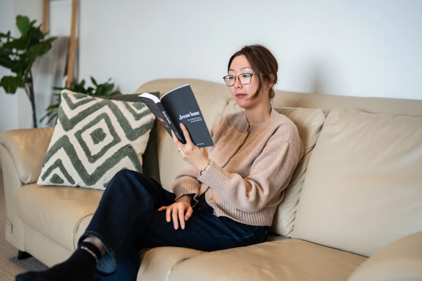 A woman reading the Dream Home paperback on a sofa at home